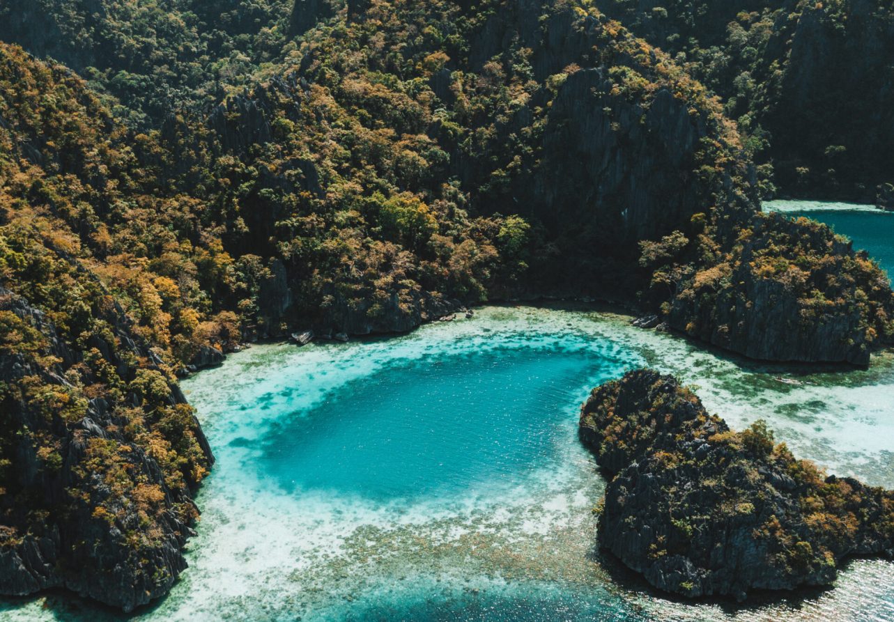 An aerial shot of the ocean surrounded by the mountains covered in greens